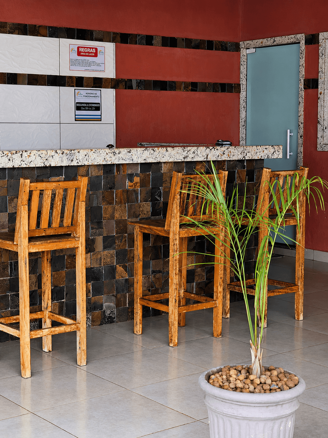 Balcão da área gourmet com banquetas de madeira, granito e plantas
