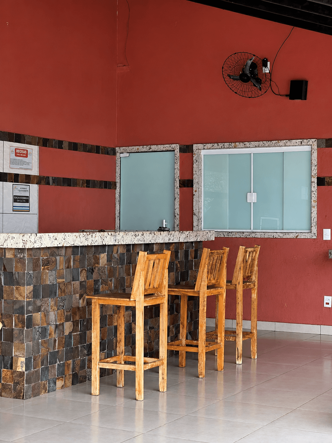 Balcão lateral da área gourmet da Vila Agostinis com banquetas de madeira e ventilador de parede.