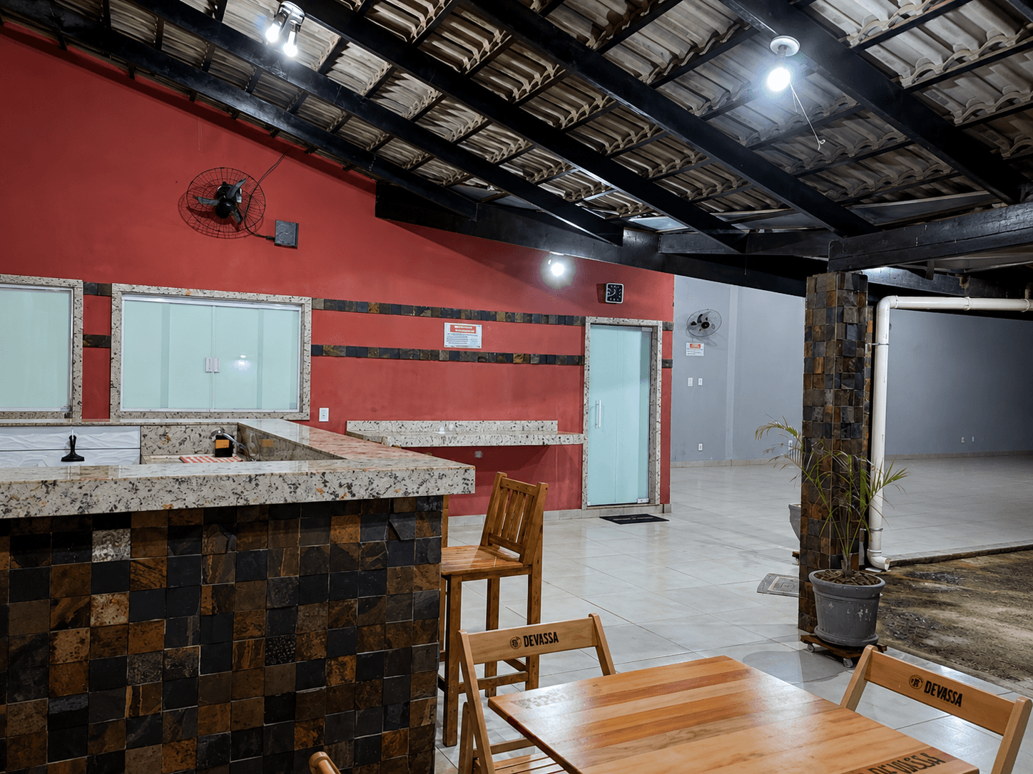 Área gourmet da Vila Agostinis iluminada à noite, com balcão e mesas de madeira.