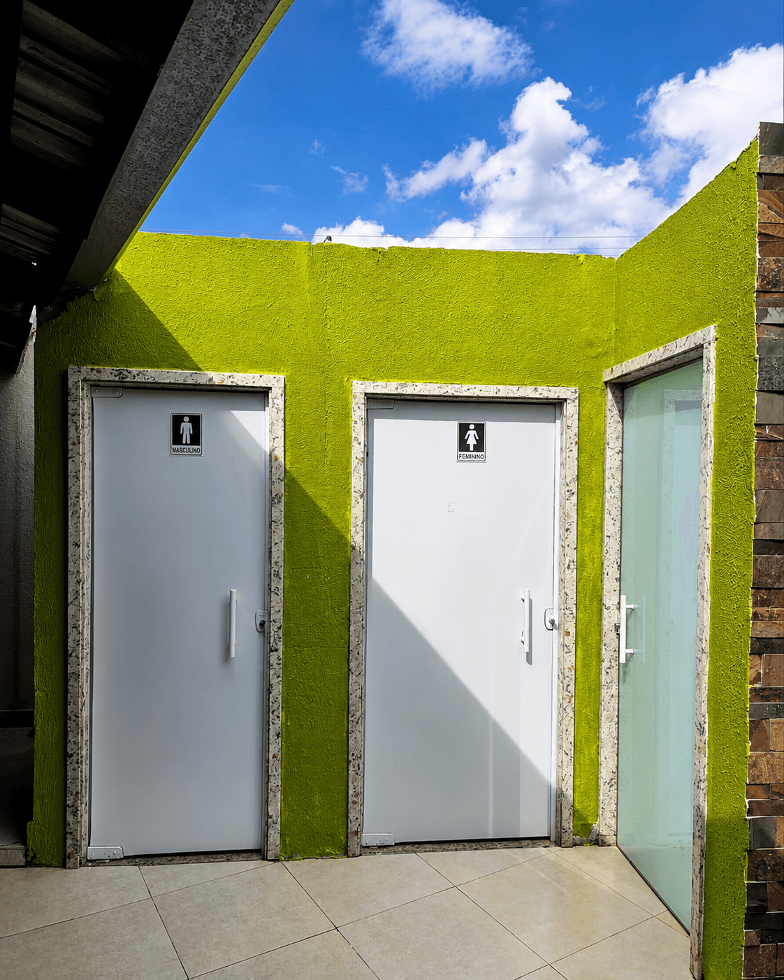 Dois acessos de banheiro identificados como masculino e feminino, junto a uma porta de vidro em parede verde-limão.