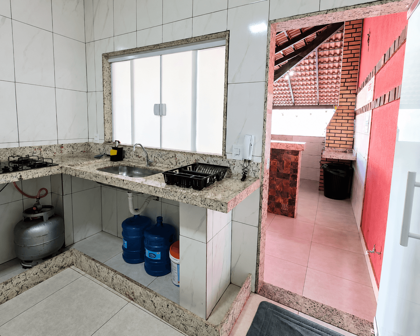 Cozinha de apoio da Vila Agostinis com pia, botijão de gás e vista para a área gourmet ao fundo.