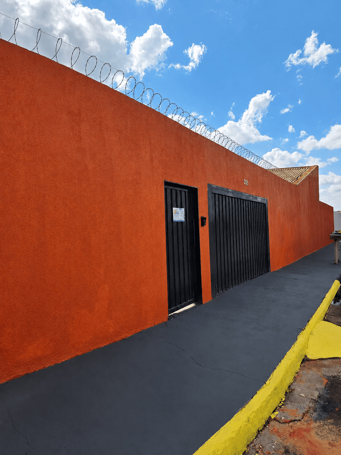 Portão preto de entrada da Vila Agostinis, em muro laranja com arame farpado no topo.