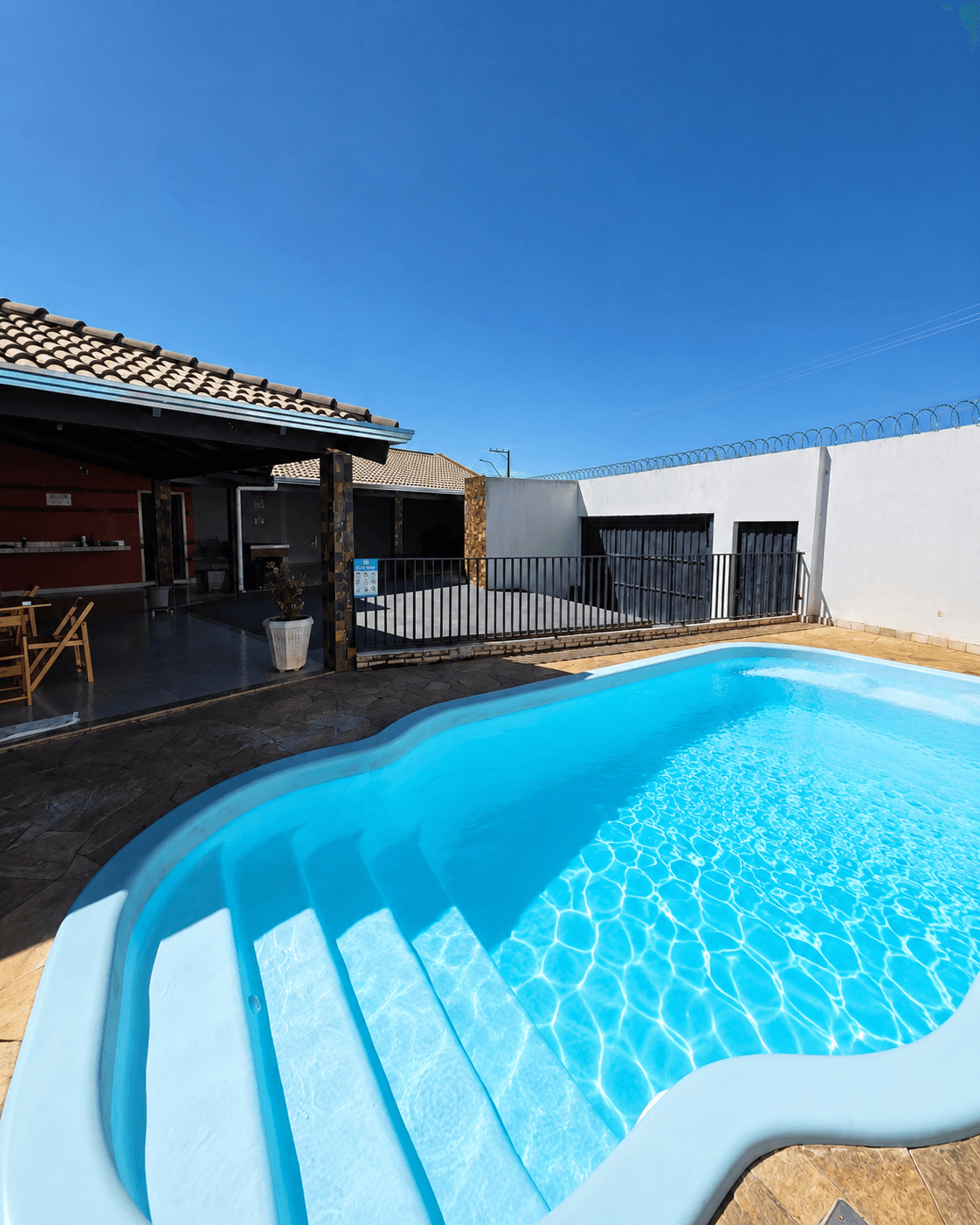 Piscina da Vila Agostinis com escada de acesso à água, sob céu azul e área coberta ao fundo