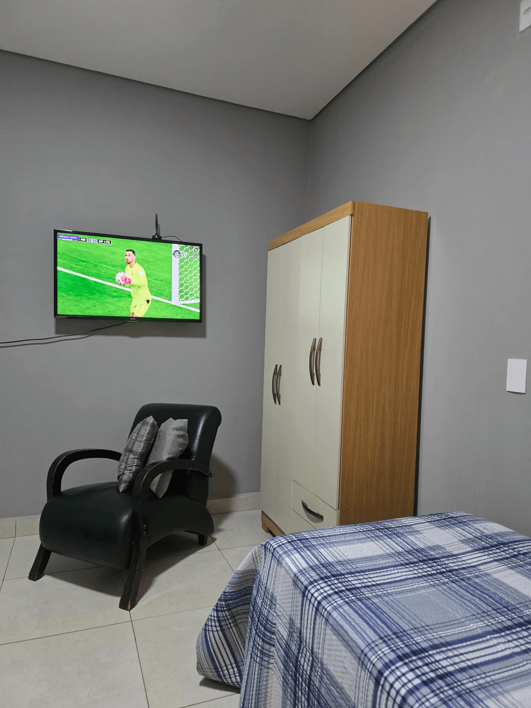 Quarto de apoio da Vila Agostinis com televisão na parede, poltrona de couro e armário.