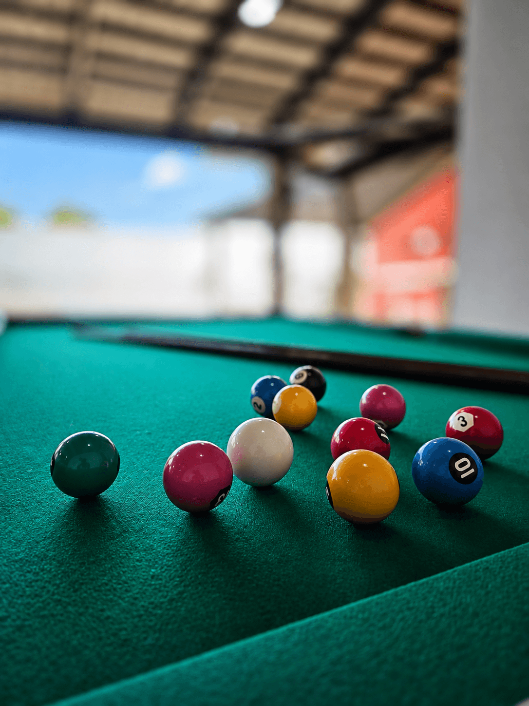 Bolas de sinuca coloridas em primeiro plano sobre o tecido verde da mesa.